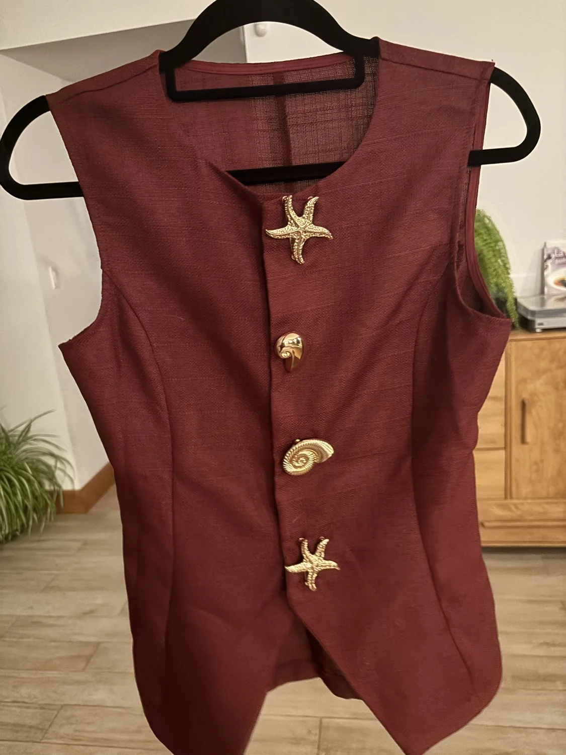Un gilet bordeaux avec des boutons dorés en forme de coquillages et d’étoiles de mer